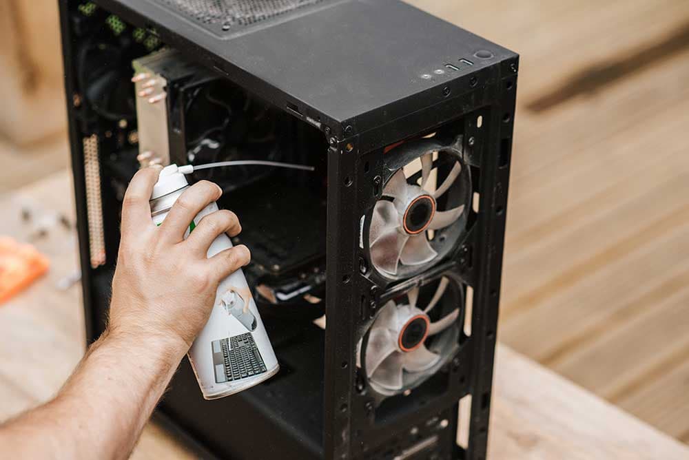 Hands cleaning dust from the internals of an open desktop PC with compressed air and a soft